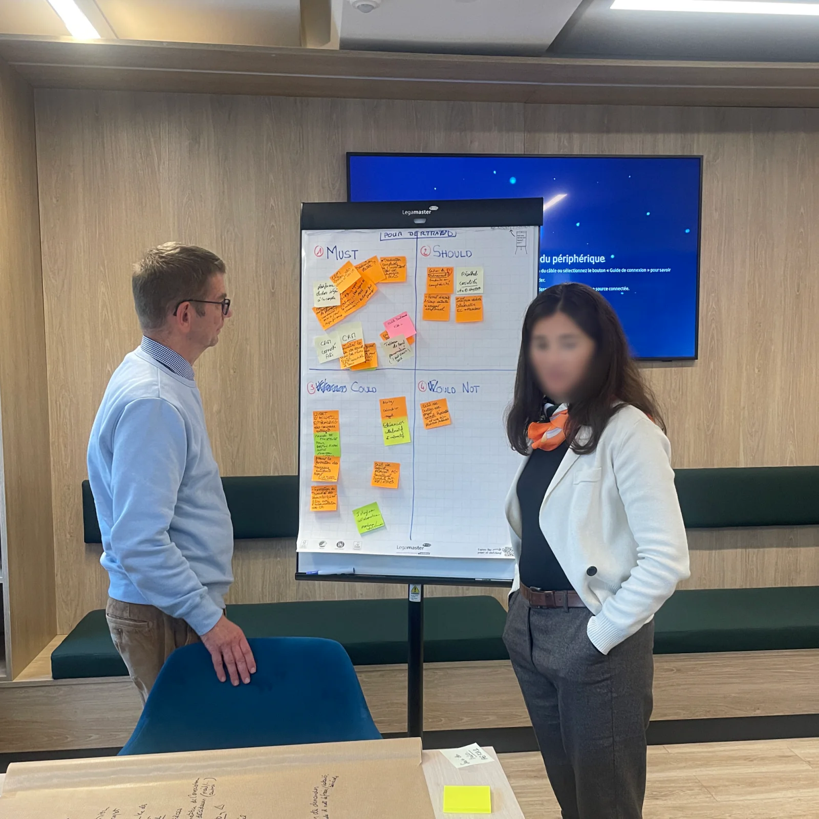 Atelier de priorisation : deux personnes devant un tableau de post-its classés en quatre colonnes, de l'indispensable à l'exclu.